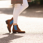 Brown ankle boots with blue accents worn by a person on a road.