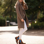 Woman wearing a brown checkered coat and white pants walking outdoors.