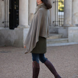 Woman wearing a beige cape and brown knee-high boots walking outdoors.