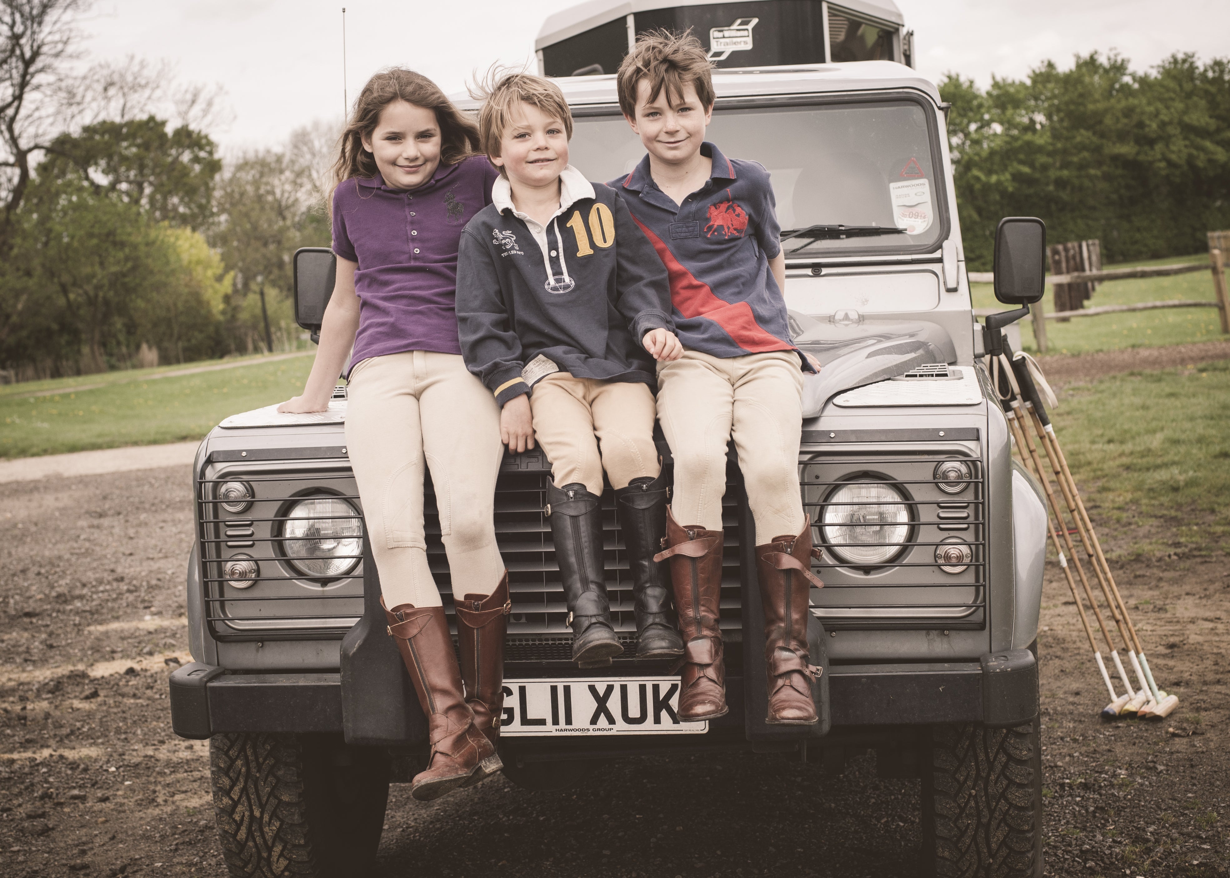 Three children sitting on a Land Rover wearing Polo boots