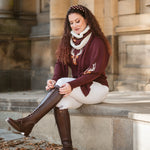 Woman sitting on steps wearing a burgundy sweater, white pants, and knee-high brown boots.