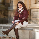 Woman sitting on steps wearing a burgundy sweater, white pants, and knee-high brown boots.