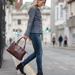 Woman walking on a city street holding a brown leather bag with Heeled Navy Suede Ankle Boots