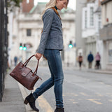 Woman walking on a city street holding a brown leather bag with Heeled Navy Suede Ankle Boots