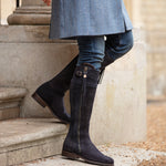 Person wearing navy suede knee-high boots and a blue coat on stone steps.